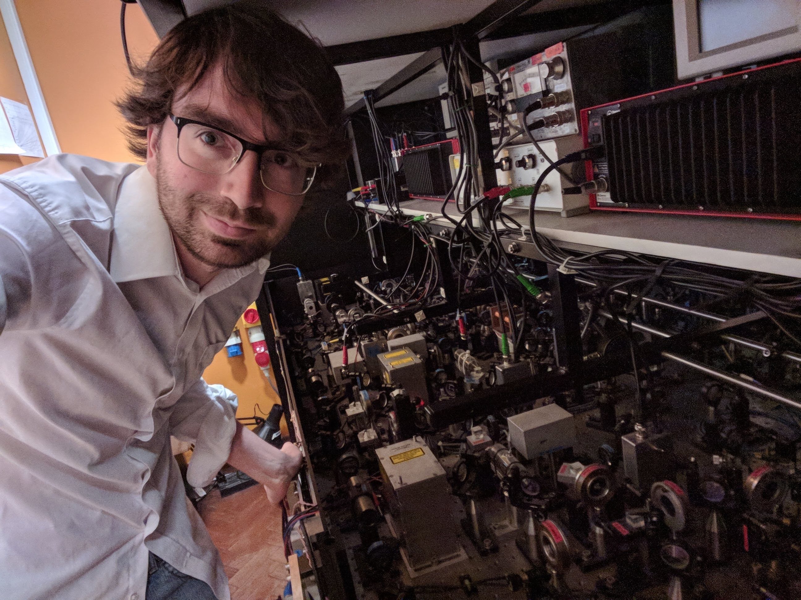 Dr Phil Gregory next to an optical bench showing some of the optical components needed to realise a state-of-the-art cold molecule experiment.